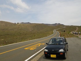 一本道の脇に停まる黒い軽自動車