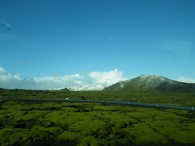 緑の苔の草原の奥に見える山と青空