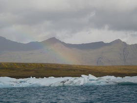 氷河が浮かぶ湖の奥に虹がかかる山