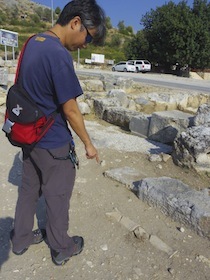 地面に埋もれる水道管の遺跡を指差す男性