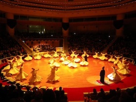 円形の劇場で白い衣装を着て踊る人たち