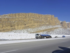 雪が積もった岩山の前を走る大型トラック