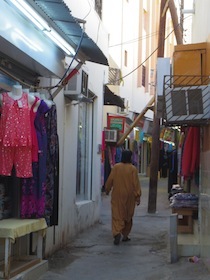 女性服が並ぶ店の脇の細い小道を歩く人