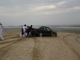 砂浜で車を押す人たち