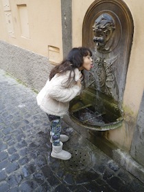 街角の水飲み場で水を飲む少女