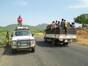 荷台に大勢の人を乗せたトラックとその横で上で作業する人がいる車