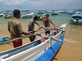 海辺で青と白のボートを運ぶ三人の男性